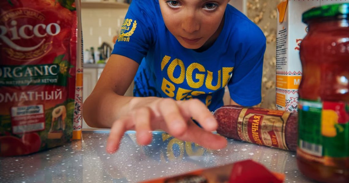 Young boy reaching into refrigerator for a snack. Close-up view indoors.