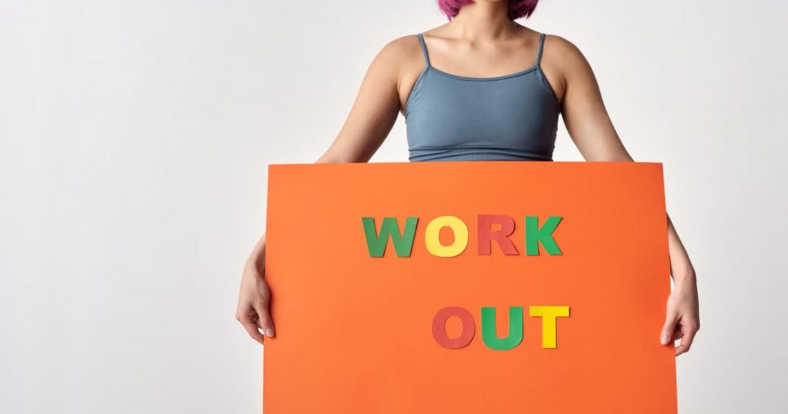 Woman with short hair holding a vibrant 'Work Out' sign on a white background.